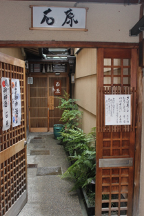 A tsubo-niwa, the small enclosed courtyard garden at the middle of a machiya, planted with moss and ferns against a rendered wall, with stone underfoot.